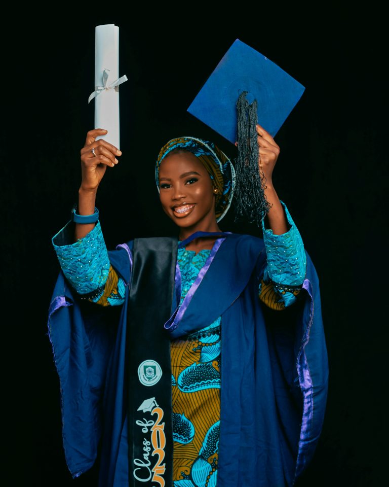 A female graduate smiling while holding her her graduation cap and ceremonial baton.