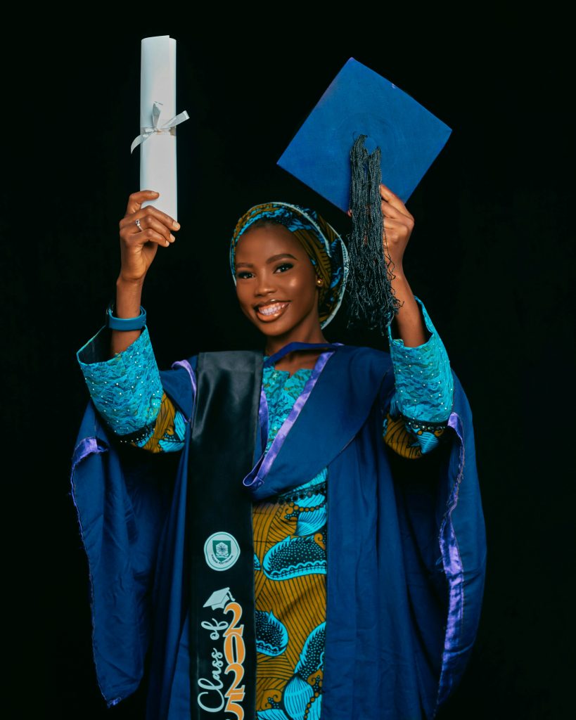 A female graduate smiling while holding her her graduation cap and ceremonial baton.